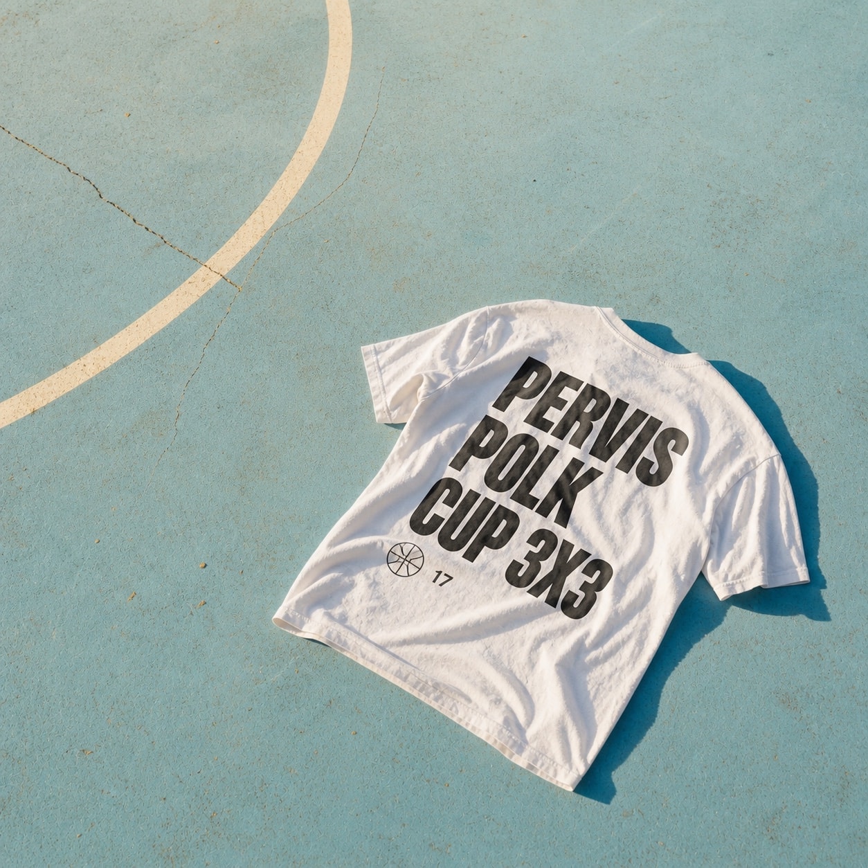 Pervis Polk Cup T-shirt photographed on a sunlit outdoor basketball court